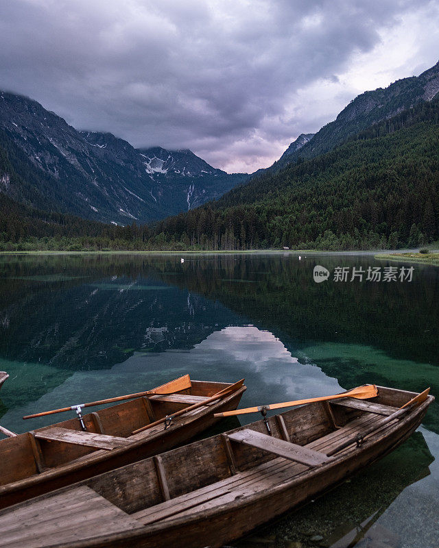 As the sun sets over the serene Jägersee in Austria, a rowing boat gently floats in the foreground, adding a sense of tranquility and calmness to the already beautiful landscape.